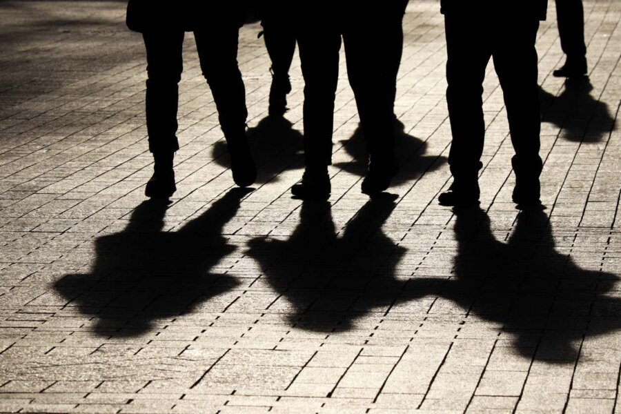 Silhouettes of a group of people; their shadows fall on the stone pavers in front of them as they walk.